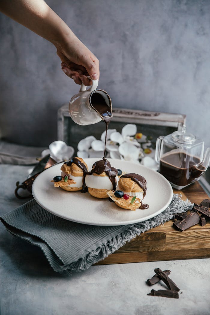 our-journey-02 Profiteroles topped with chocolate sauce being poured. A tempting dessert perfect for sweet lovers.